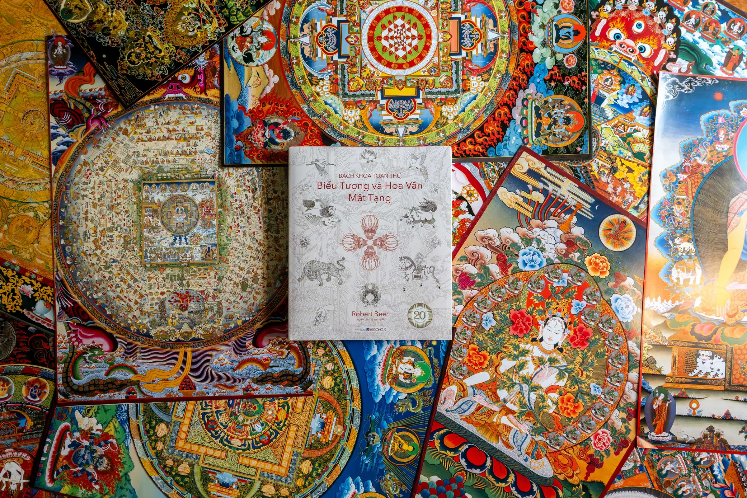 The Vietnamese edition of the Encyclopedia of Tibetan Symbols and Motifs against a backdrop of thangkas